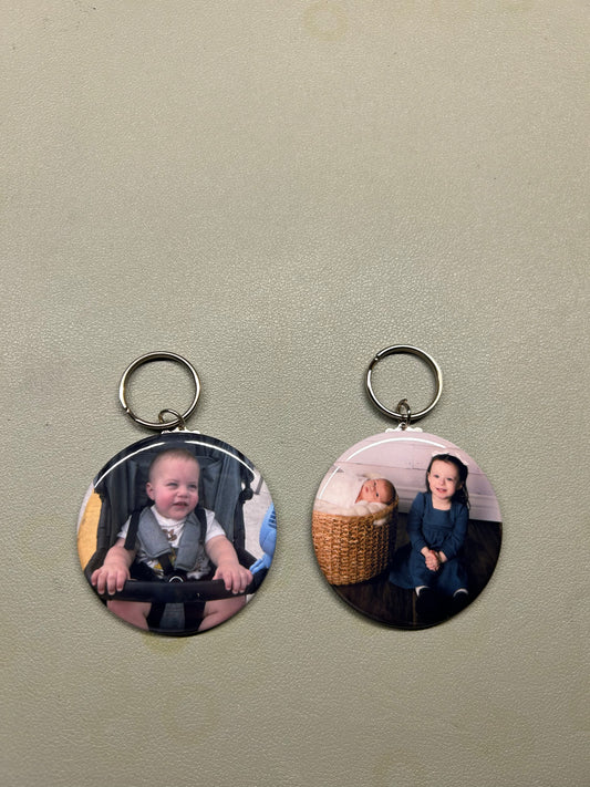 Two circular keychains with photos of children on a beige surface